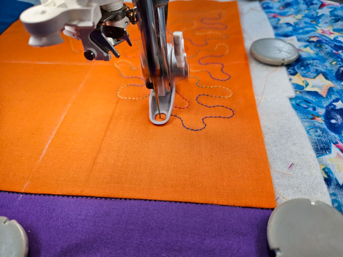 An orange square of fabric with a machine embroidery presser foot; Husqvarna VIKING DESIGNER EPIC 3