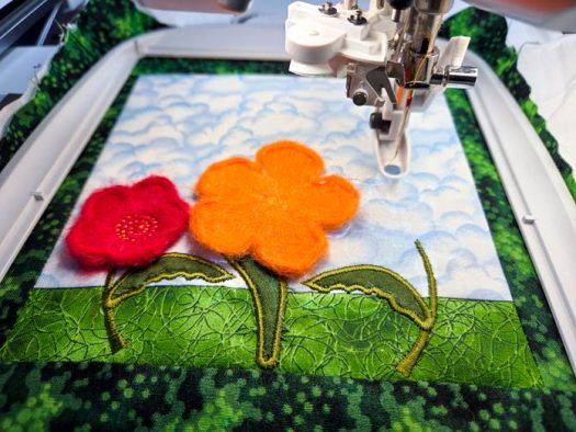 A red and orange felt flower on a blue and green background