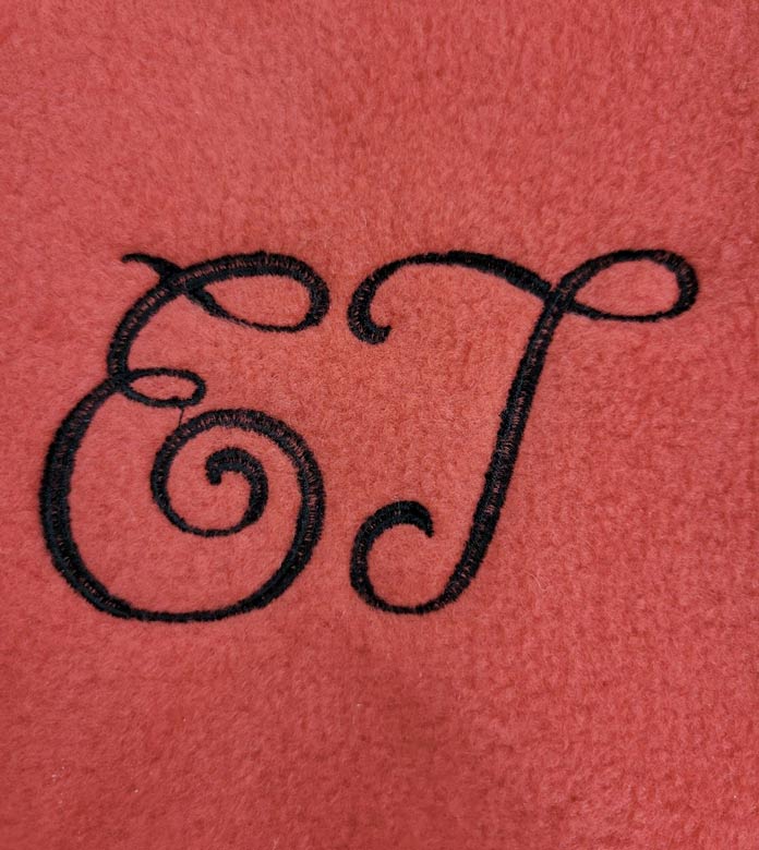 The letters E and T in black thread on a piece of red fleece