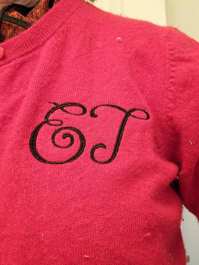 A two-letter monogram in black stitching on a red sweater