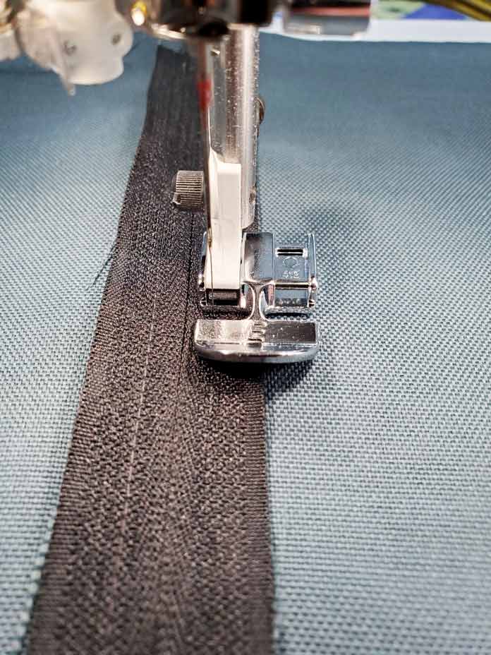 A metal presser foot on a sewing machine stitching a black zipper in place. Husqvarna Viking Designer Sapphire 85, Inspira EZ Snip Curved Scissors