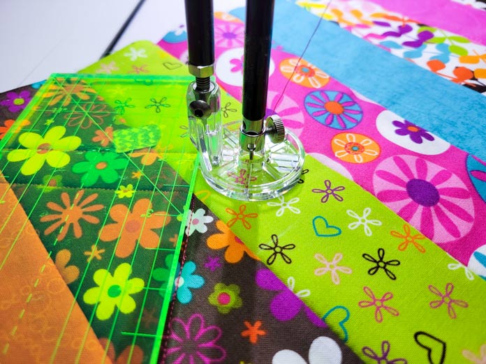 A neon green ruler and a plastic foot on a stationary quilting machine with brown, green, and pink floral fabric; Husqvarna Viking PLATINUM™ Q160, Husqvarna Viking Echo Feet Set
