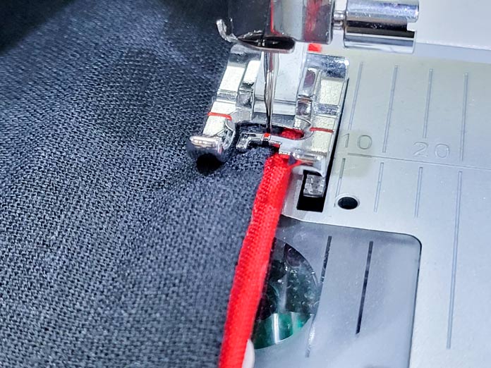 A red strip on the edge of a black fabric under the presser foot of a sewing machine; Husqvarna Viking Tribute 150C