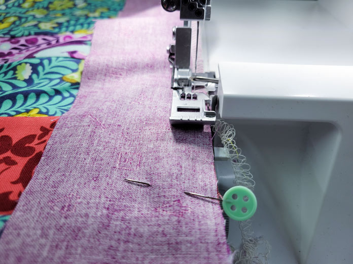 A pin on purple fabric in front of a serger foot; Husqvarna Viking Amber Air S600