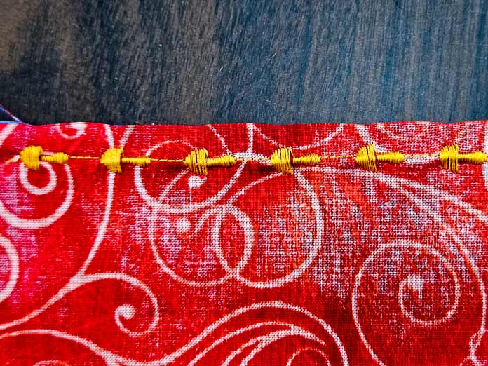 A line of mushroom-shaped stitches in yellow thread on orange fabric; Husqvarna VIKING DESIGNER EPIC 3