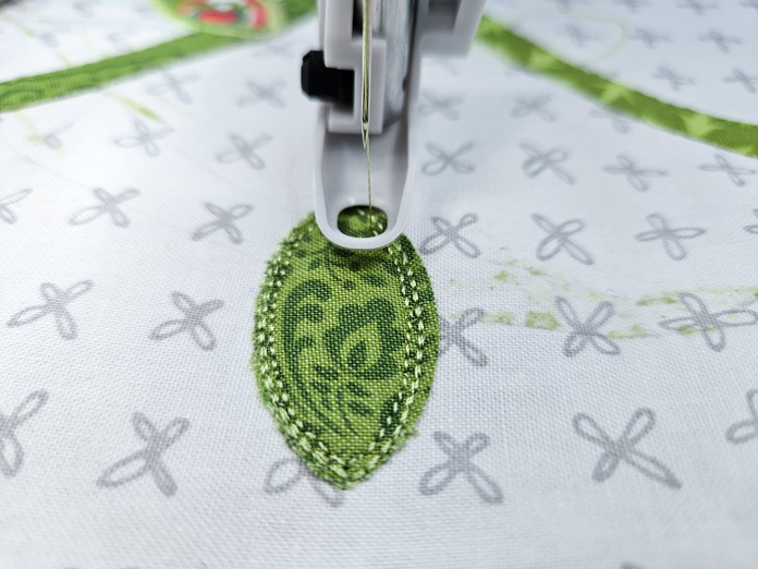 A green petal with rows of stitching on the perimeter on a white fabric