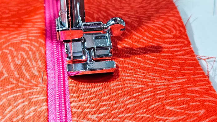 The Husqvarna VIKING ONYX 25 metal zipper foot sewing a pink zipper on orange fabric
