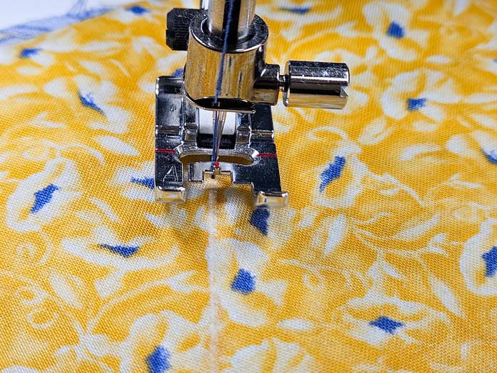A metal presser foot on yellow fabric