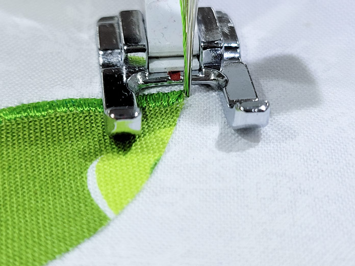 A metal open-toe foot on a sewing machine on a pointy green fabric; Husqvarna Viking Tribute 150C