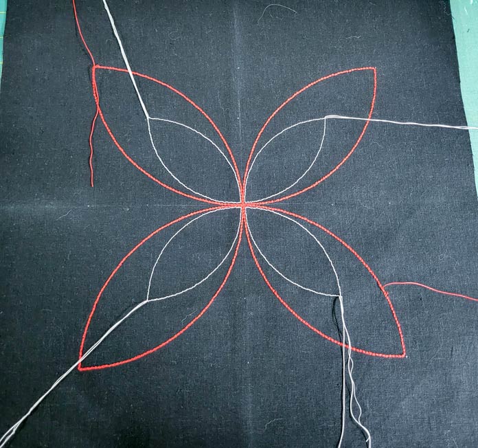 A four-petal flower with red and white thread on black fabric; Gütermann topstitching threads