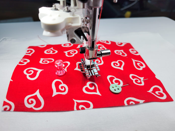 White hearts on a red fabric under a sewing machine presser foot; Husqvarna Viking Designer EPIC 2