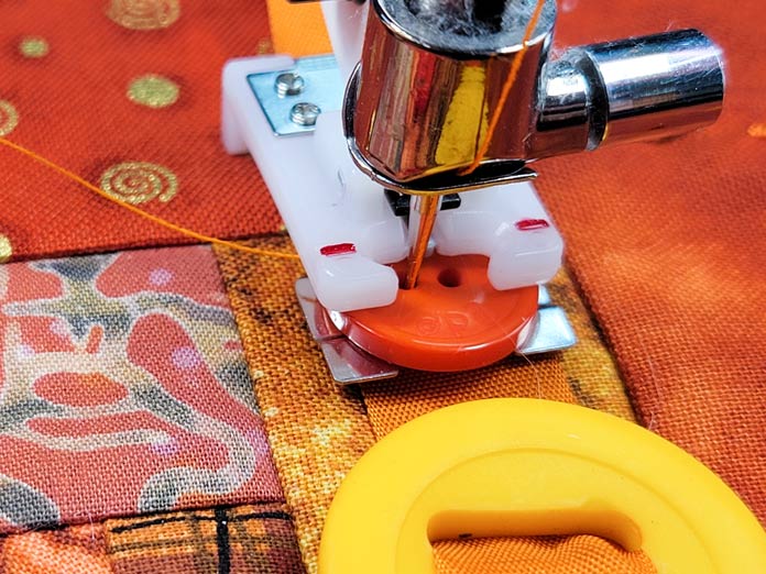 An orange button in a plastic presser foot on a sewing machine; Husqvarna Viking Button Foot with Placement Tool, Husqvarna Viking DESIGNER EPIC 2