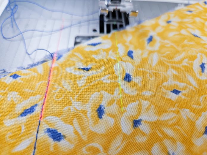 A red projection line and a green stitch preview line on yellow fabric