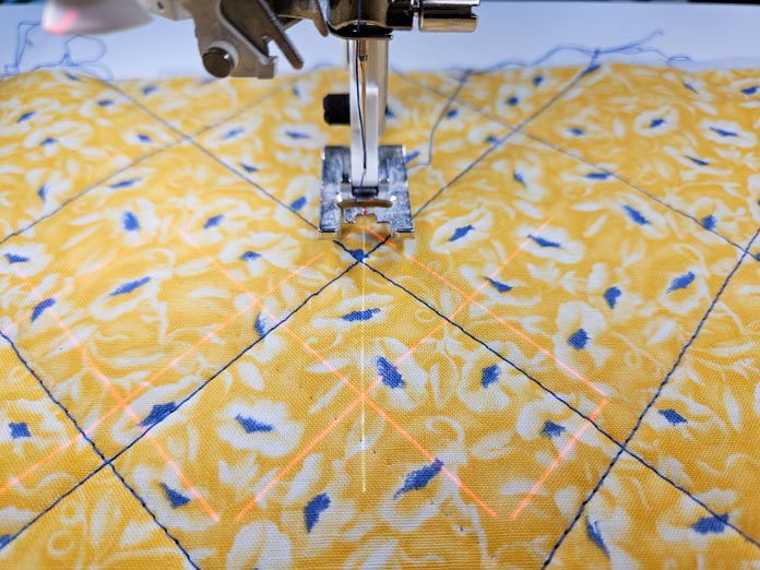 Blue lines of stitching and a red grid on yellow fabric with a metal presser foot