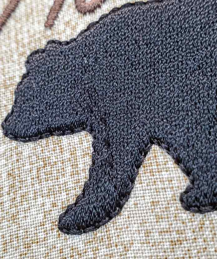 A bear embroidered in black thread on a tan fabric