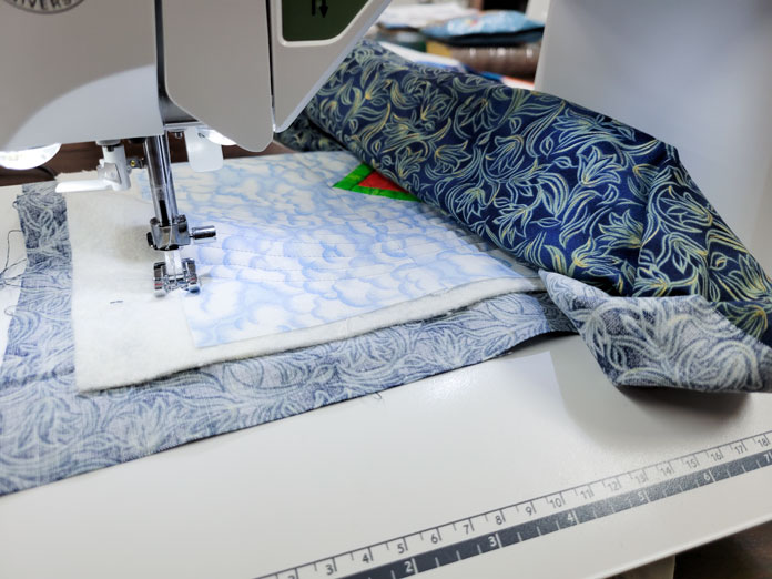 A small quilt rolled up under the arm of a sewing machine; Husqvarna Viking Tribute 150C
