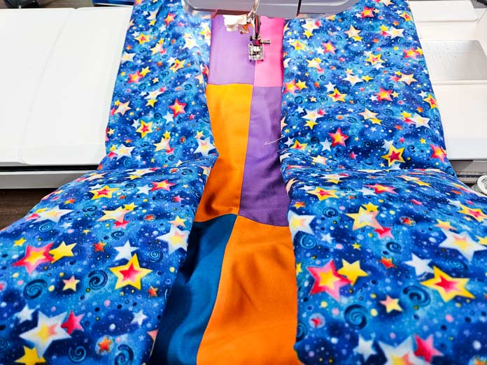 A multi-color quilt top under the presser foot of a sewing machine; Husqvarna VIKING DESIGNER EPIC 3