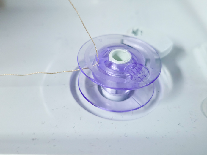 A purple bobbin with a beige thread through a slot in the face
