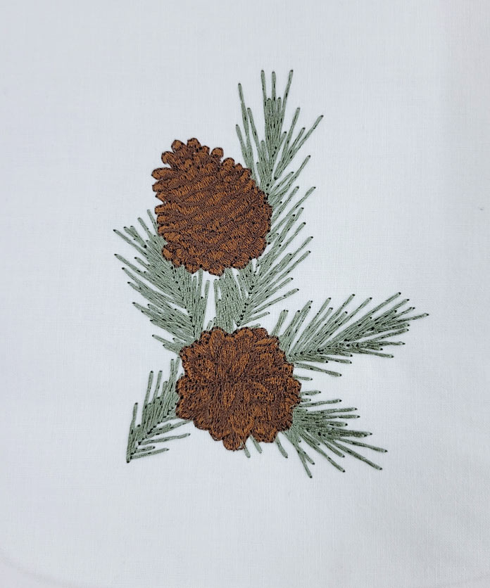 A pinecone stitched in machine embroidery with green and brown thread on white fabric
