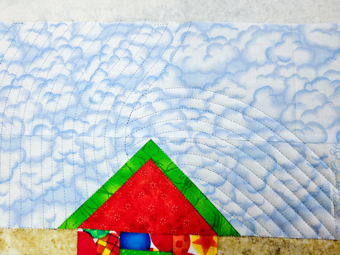 Blue sky over a colorful house in a quilt with lines of blue stitching