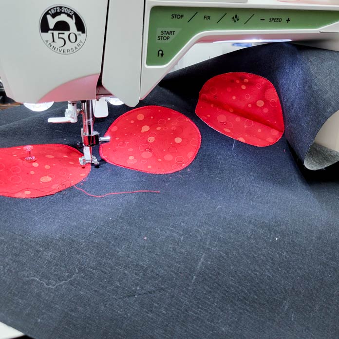 Three red circles on a black fabric under the presser foot of a sewing machine; Husqvarna Viking Tribute 150C