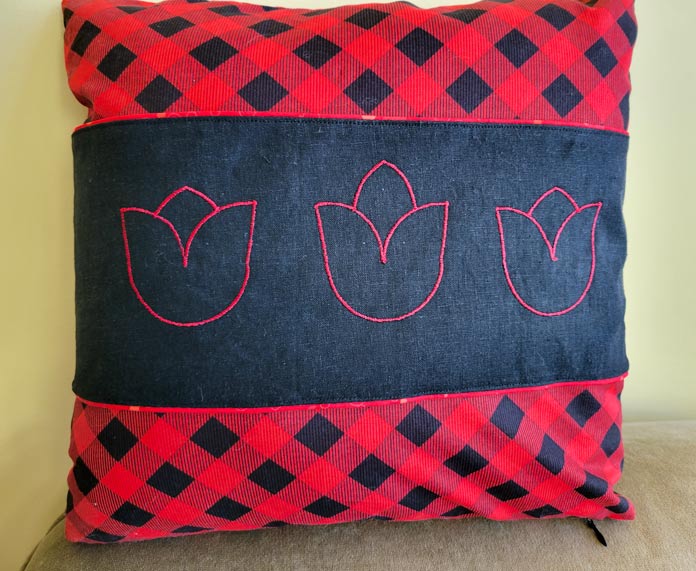 Three red tulip shapes on a black fabric band on a red and black plaid cushion