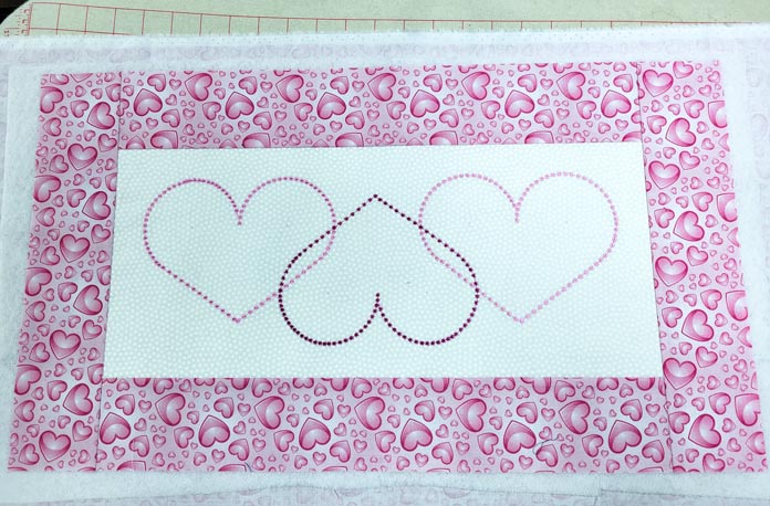 Three heart outlines on white fabric with pink fabric