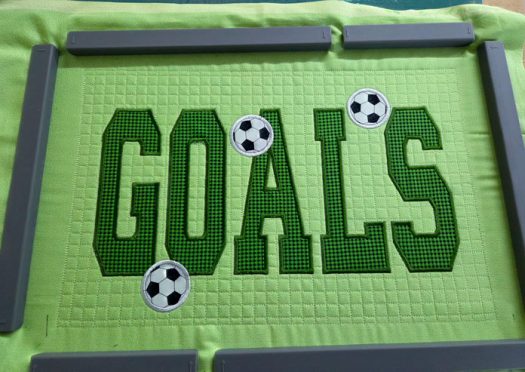 Three fabric soccer balls on green fabric with the word GOALS