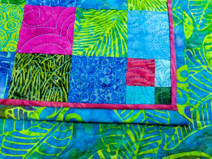 A teal, green, and pink quilt with pink piping