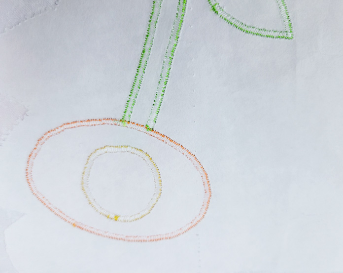 A circle of yellow stitching inside an oval of orange stitching