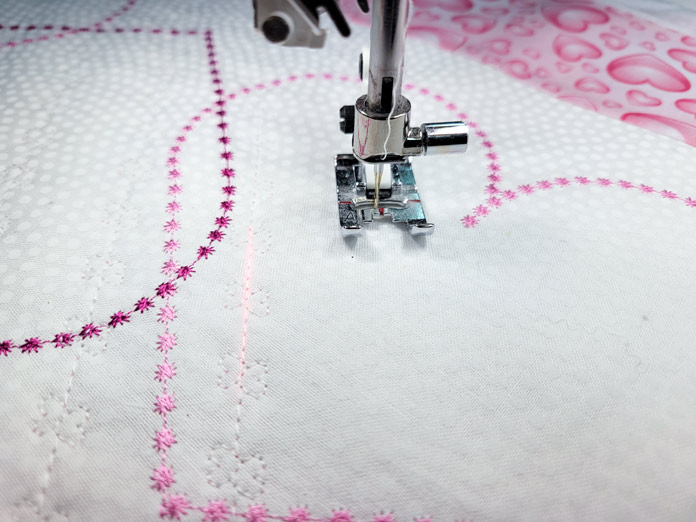 Pink stitches on white fabric with a sewing machine presser foot; Husqvarna Viking DESIGNER EPIC 2