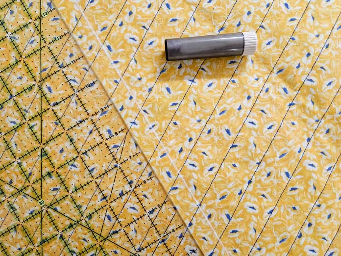 A quilter's ruler, a chalk marking tool and a white chalk line, on yellow fabric