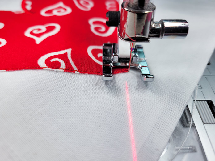 A red and white heart on white fabric with a red laser; Husqvarna Viking Designer EPIC 2