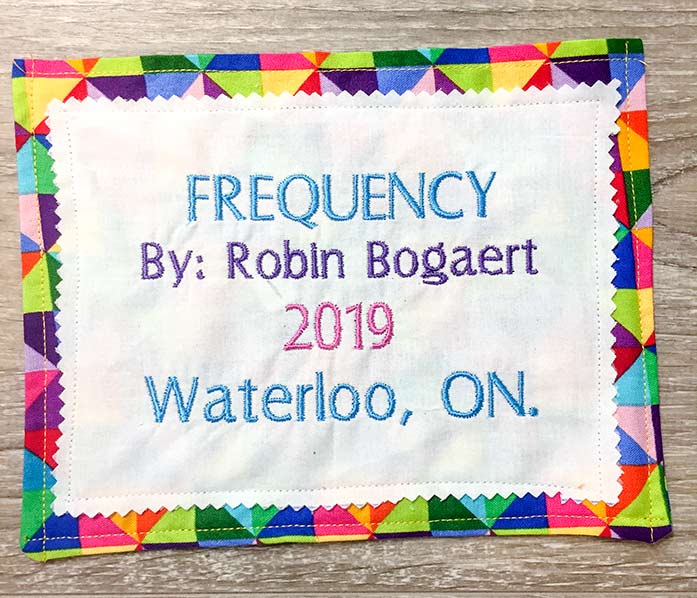 A colorful machine embroidered quilt label made with Sulky Cut-Away Soft 'n Sheer Stabilizer, Gütermann Dekor Rayon thread and Fabric Creations 100% Cotton.
