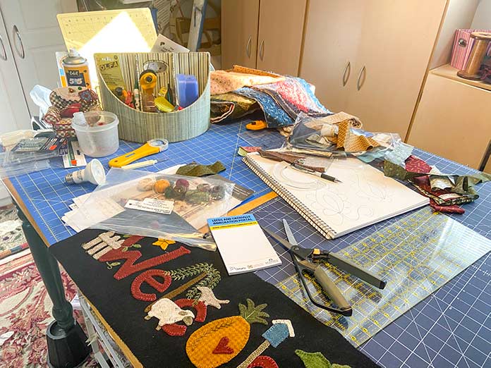 Christine’s cutting table covered with rulers, rotary cutters, pens, pencils and projects.