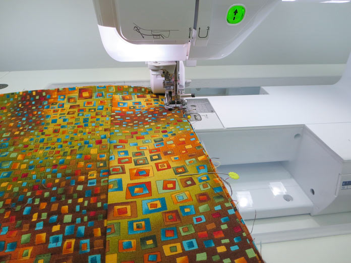 The hanging sleeve is stitched to the back of a quilt with a sewing machine. Brother Innov-ís BQ3050 sewing and quilting machine, MuVit Digital Dual Feed Foot, SA195 MuVit Open-Toe Dual Feed Foot, Mary Ellen’s Best Press, Banyan Batiks