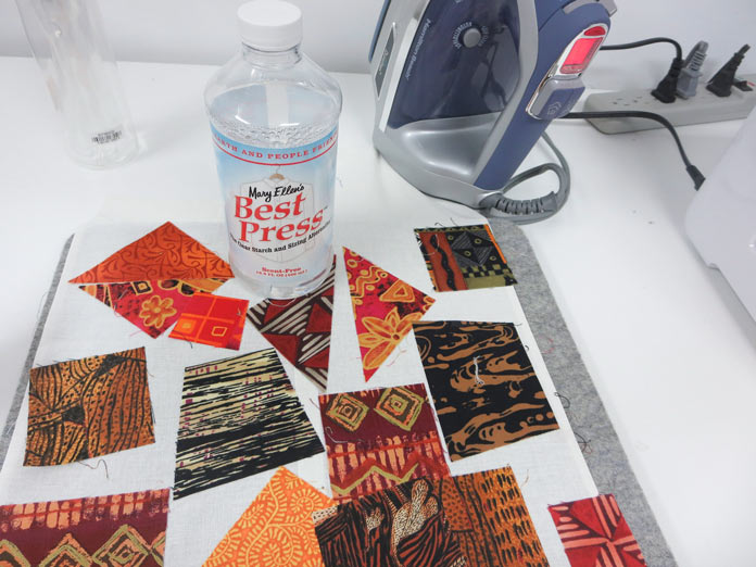 Fabric pieces, and iron and a bottle of Mary Ellen’s Best Press sitting on a pressing table. Brother Innov-ís BQ3050 sewing and quilting machine, MuVit Digital Dual Feed Foot, SA195 MuVit Open-Toe Dual Feed Foot, Mary Ellen’s Best Press, Banyan Batiks