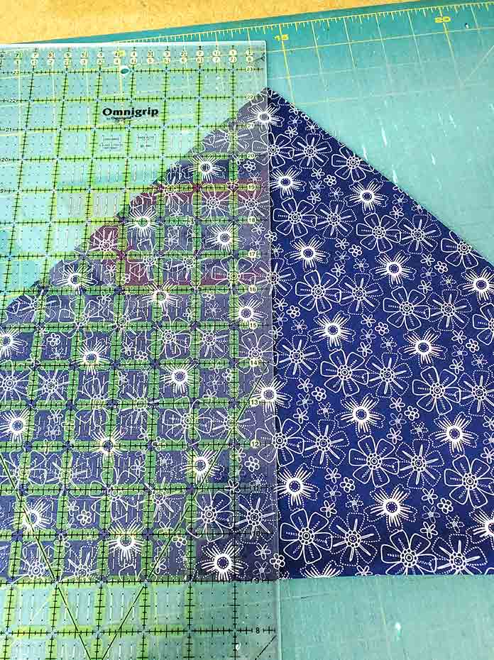 A quilter’s ruler placed on a large blue and white triangle of fabric. Spectrum QAL2020 made with the Blue Stitch collection by Riley Blake Designs