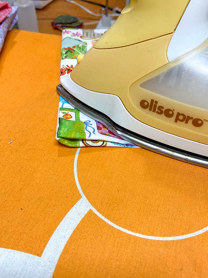 The sewn rectangle shown being pressed by a yellow iron on an orange iron board cover.