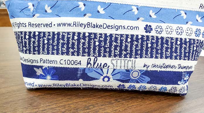 The selvages of the Blue Stitch collection by Riley Blake Designs start at the bottom of the side of the zippered pouch. Blue Stitch collection by Riley Blake Designs, Husqvarna Viking EPIC2 sewing and embroidery machine, Husqvarna Viking Open Toe Foot, Singer Steam Press ESP2