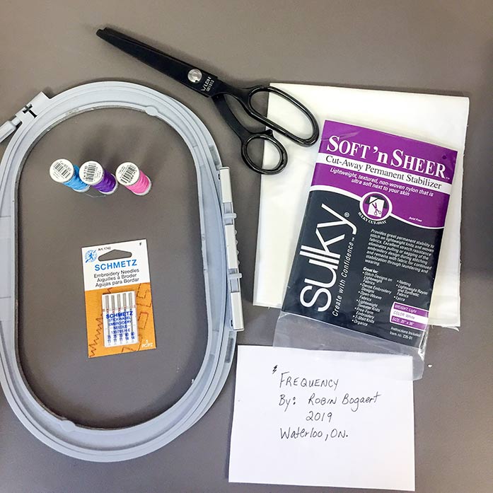 Supplies needed to make a machine embroidered label, including an embroidery hoop, Sulky Cut-Away Soft’n Sheer Permanent Stabilizer, Gütermann Dekor Rayon Thread, Schmetz Machine Embroidery Needles, LDH 9" Pinking Sheers and your label written on paper.