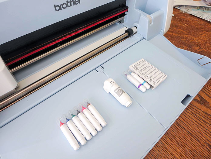 The drawing pen set comes with the Brother ScanNCut SDX225, Brother BQ3050 sewing machine, Brother brayer, Brother spatula, Brother standard tack cutting mat, color pen set, Brother universal pen holder