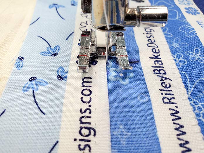 Stitching the selvages of the Blue Stitch collection by Riley Blake Designs to the foundation fabric. Blue Stitch collection by Riley Blake Designs, Husqvarna Viking EPIC2 sewing and embroidery machine, Husqvarna Viking Open Toe Foot, Singer Steam Press ESP2