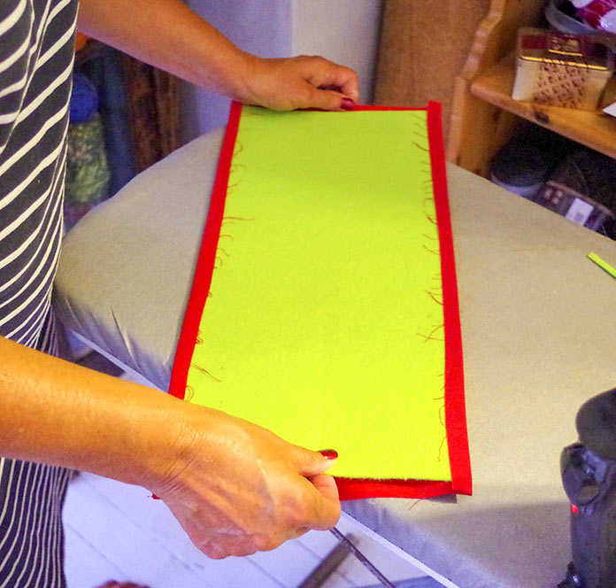 The light green rectangle of felt is being centered on the red bottom of the bag. You can see a ½” border on all sides of the felt that will be folded in or sewn into the bag to make the bottom. 