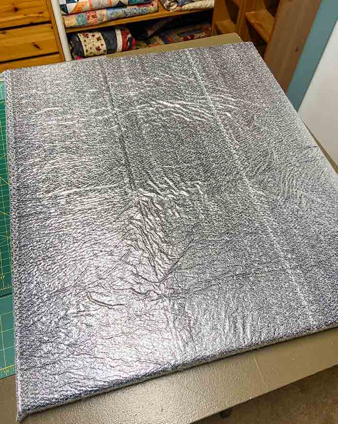 The shiny side of the UNIQUE Quilting Therm Fleece provides protection from hot surfaces up to 390°F (200°C). UNIQUE Wool Pressing Mat, Oliso M2Pro Mini Project Iron, Oliso Pro TG1600 Smart Iron, UNIQUE Quilting Therm Fleece, Fairfield Toasty Cotton Natural Cotton Quilt Batting
