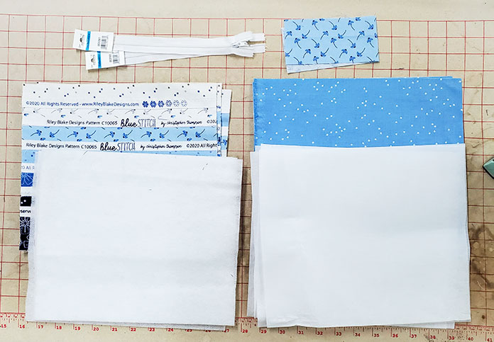 The supplies for the zippered pouches made with the Blue Stitch collection by Riley Blake Designs. Blue Stitch collection by Riley Blake Designs, Husqvarna Viking EPIC2 sewing and embroidery machine, Husqvarna Viking Open Toe Foot, Singer Steam Press ESP2