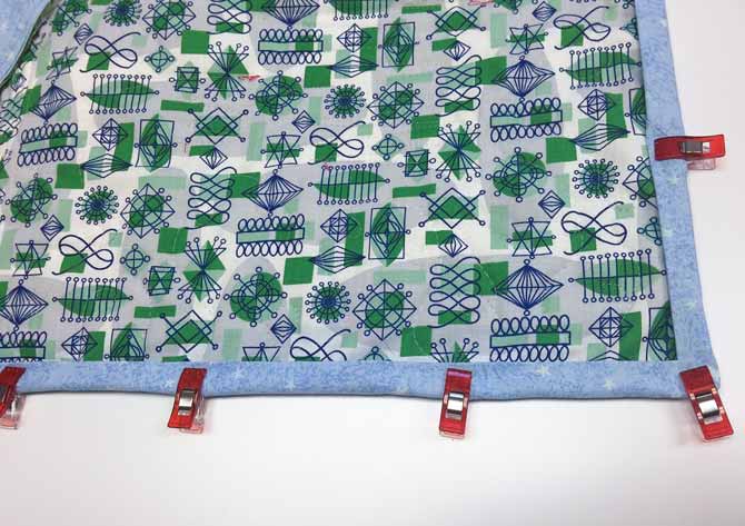 Back of quilt with binding held down by Clover Wonder Clips.
