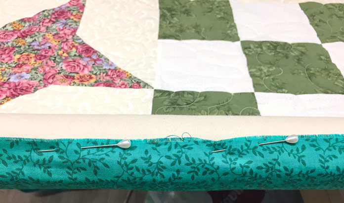 Quilt loaded onto leader rollers on my longarm machine with UNIQUE long arm pins used to secure the quilt to the roller leader fabric.