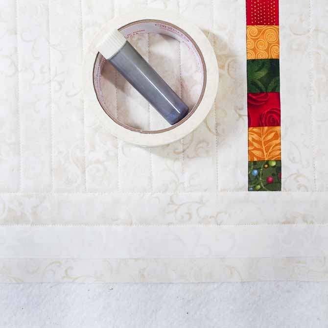 A roll of masking tape and tube of chalk liner lying on a partially quilted piece with a piece of masking tape along the bottom border