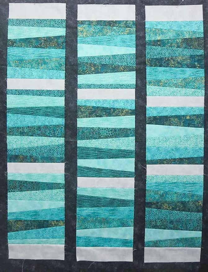 Gray Norhcott Toscana sashing strips are sewn between the wedge blocks to make three long strip sets.